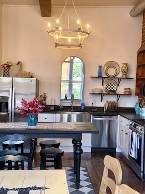 A kitchen with a central island, stainless steel appliances, a chandelier, and a large window. - Loft on Main, charming apartment in delightful Historic Downtown Jonesborough (Jonesborough)