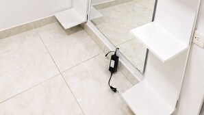 Um quarto com piso de azulejos brancos, um guarda-roupa branco com portas abertas e um espelho refletindo o ambiente.