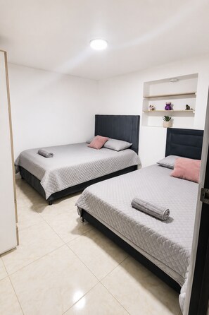 Two single beds with headboards, a white wall, a shelf with decorative items, and a door. - Experience the Authentic Colombia at Mi Rincón en Medellin (Medellín)
