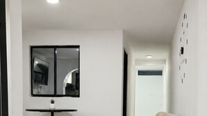 Uma sala de estar com um sofá bege, uma mesinha com uma planta em vaso e uma televisão na parede.
