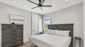A bedroom with a bed, a dresser, a nightstand, a ceiling fan, a window with blinds, and a door. - Ahoy Matey - Emerald Waters (Miramar Beach)