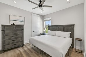 A bedroom with a bed, a dresser, a nightstand, a ceiling fan, a window with blinds, and a door. - Ahoy Matey - Emerald Waters (Miramar Beach)