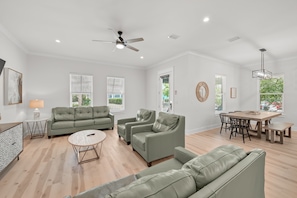 A spacious living room with a green sofa set, a dining area with a wooden table, and a ceiling fan. - Ahoy Matey - Emerald Waters (Miramar Beach)