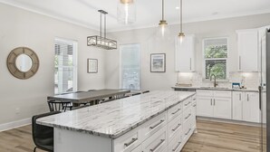 A modern kitchen with white cabinetry, a marble island, pendant lighting, and a view of the outdoors. - Ahoy Matey - Emerald Waters (Miramar Beach)