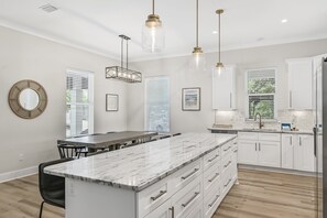 A modern kitchen with white cabinetry, a marble island, pendant lighting, and a view of the outdoors. - Ahoy Matey - Emerald Waters (Miramar Beach)