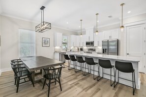 A modern kitchen with a central island, bar stools, and a dining table with chairs. - Ahoy Matey - Emerald Waters (Miramar Beach)