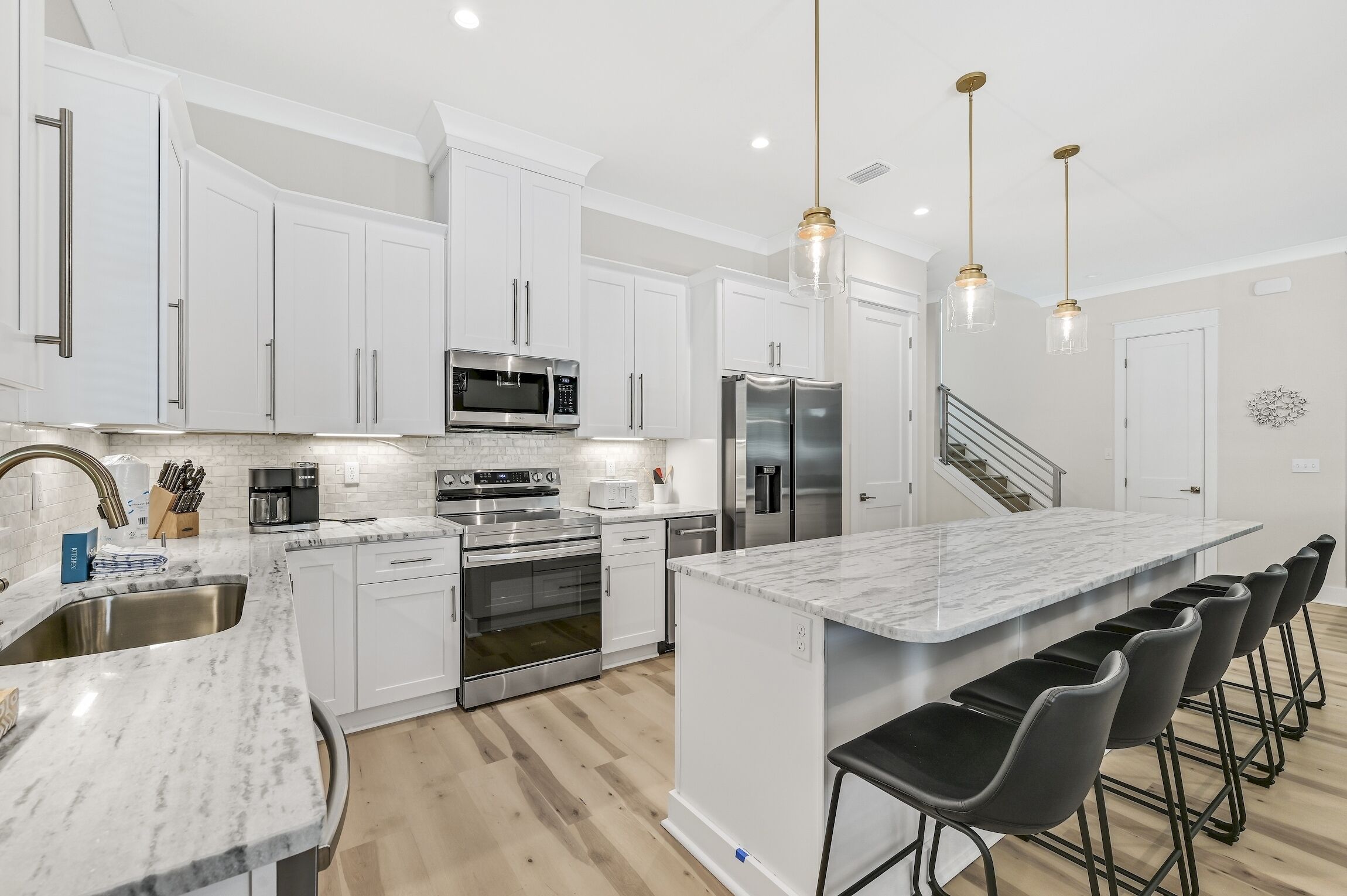 A modern kitchen with white cabinetry, stainless steel appliances, a marble island, and bar stools.
