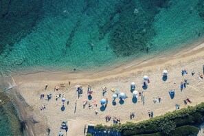 Vista aérea de una playa con agua cristalina, gente y sombrillas.