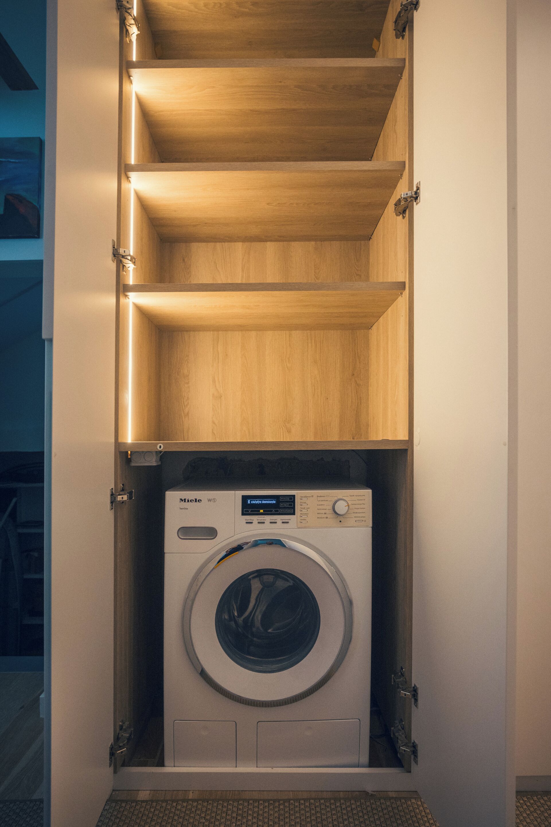 Eine kompakte Waschmaschine in einem eingebauten Schrank mit Holzregalen darüber.