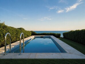 Una piscina rectangular con vista despejada al mar, rodeada de setos cuidados.