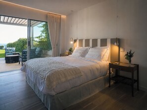 Ein Schlafzimmer mit einem großen Bett, einem Nachttisch, einer Lampe und Blick ins Freie.