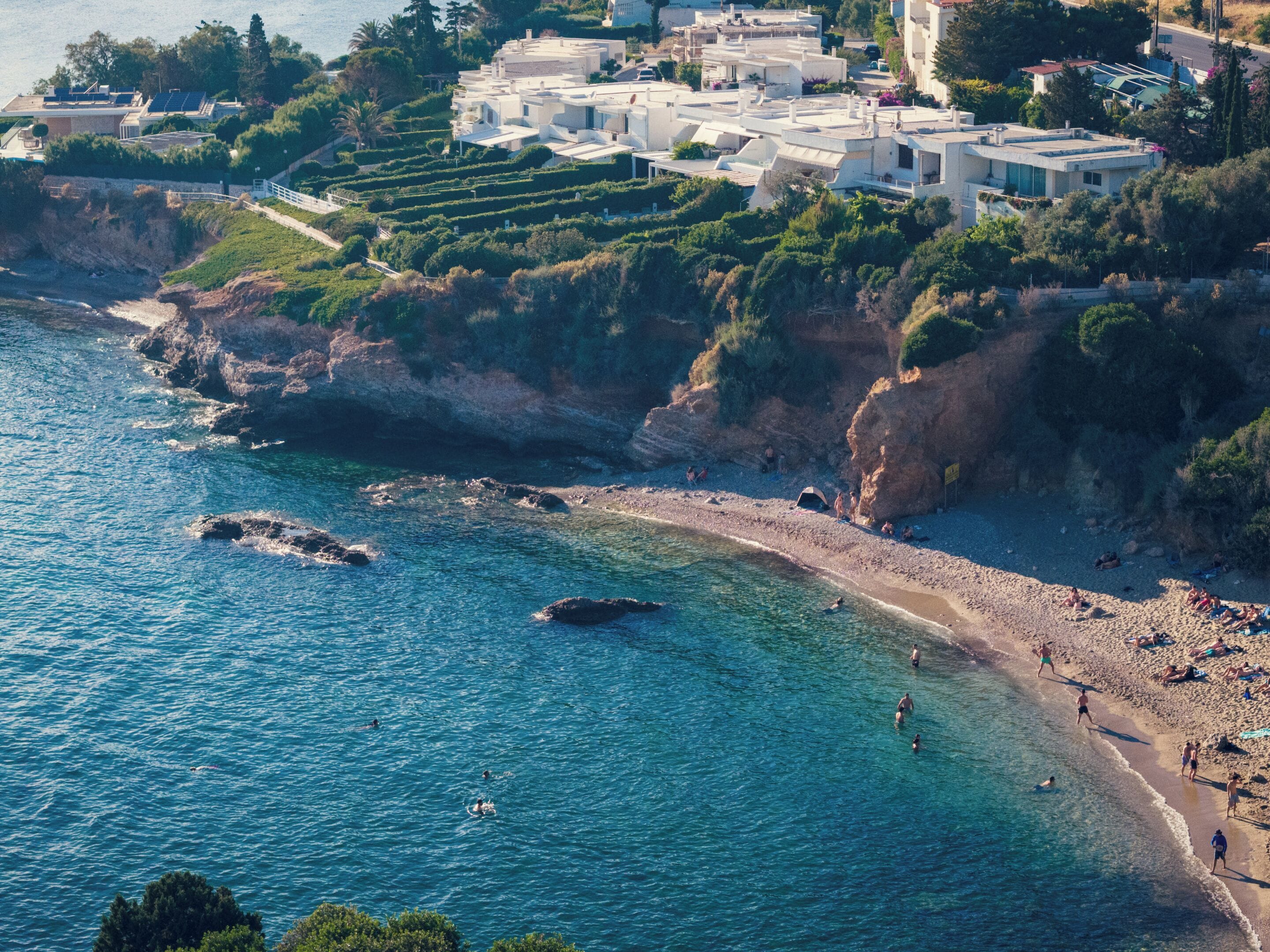 Eine Küstenlandschaft mit Strand, felsigen Klippen und einer Ansammlung von Gebäuden mit freiem Blick auf das Meer.