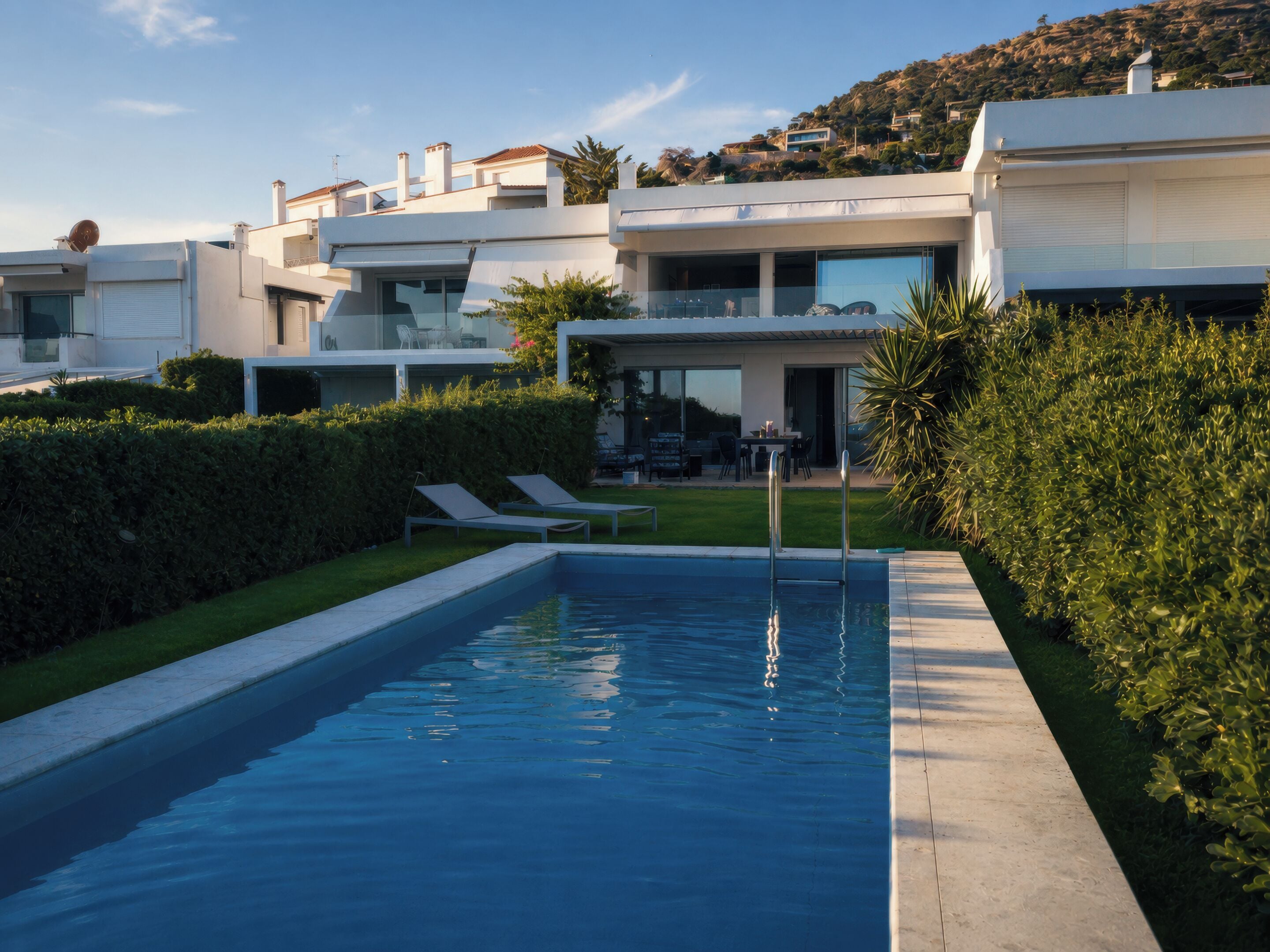 Ein moderner Pool mit klarer, blauer Wasseroberfläche, umgeben von gepflegten Hecken und einer Rasenfläche.