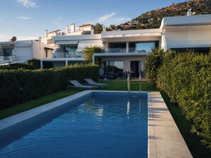 Ein moderner Pool mit klarer, blauer Wasseroberfläche, umgeben von gepflegten Hecken und einer Rasenfläche.