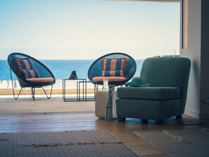 Una sala de estar moderna con vista al océano, que presenta dos sillones de mimbre, un sofá y una mesita.