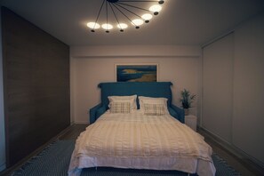 Ein Schlafzimmer mit einem Bett, einem Kopfteil, einem Gemälde, einem Nachttisch und einer Topfpflanze.