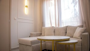 A modern living room with a sofa, a small round table, and a wall-mounted light fixture. - Kalamaria City & Sea Escape by ΜΡS (Kalamaria)
