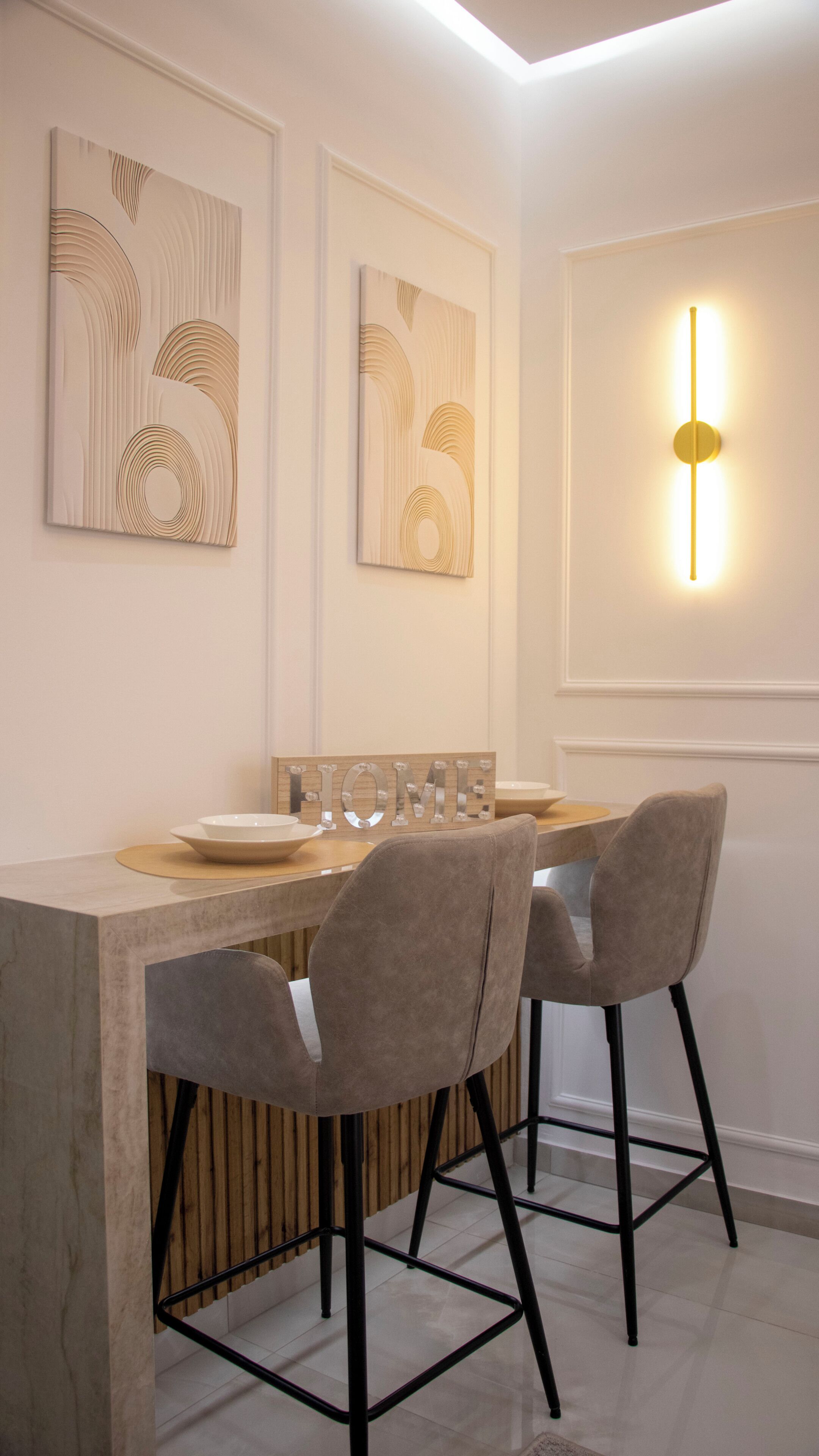 A modern dining area with a wooden table, two grey upholstered chairs, and wall-mounted artwork.