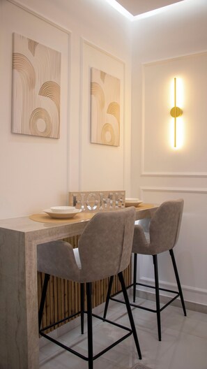 A modern dining area with a wooden table, two grey upholstered chairs, and wall-mounted artwork. - Kalamaria City & Sea Escape by ΜΡS (Kalamaria)