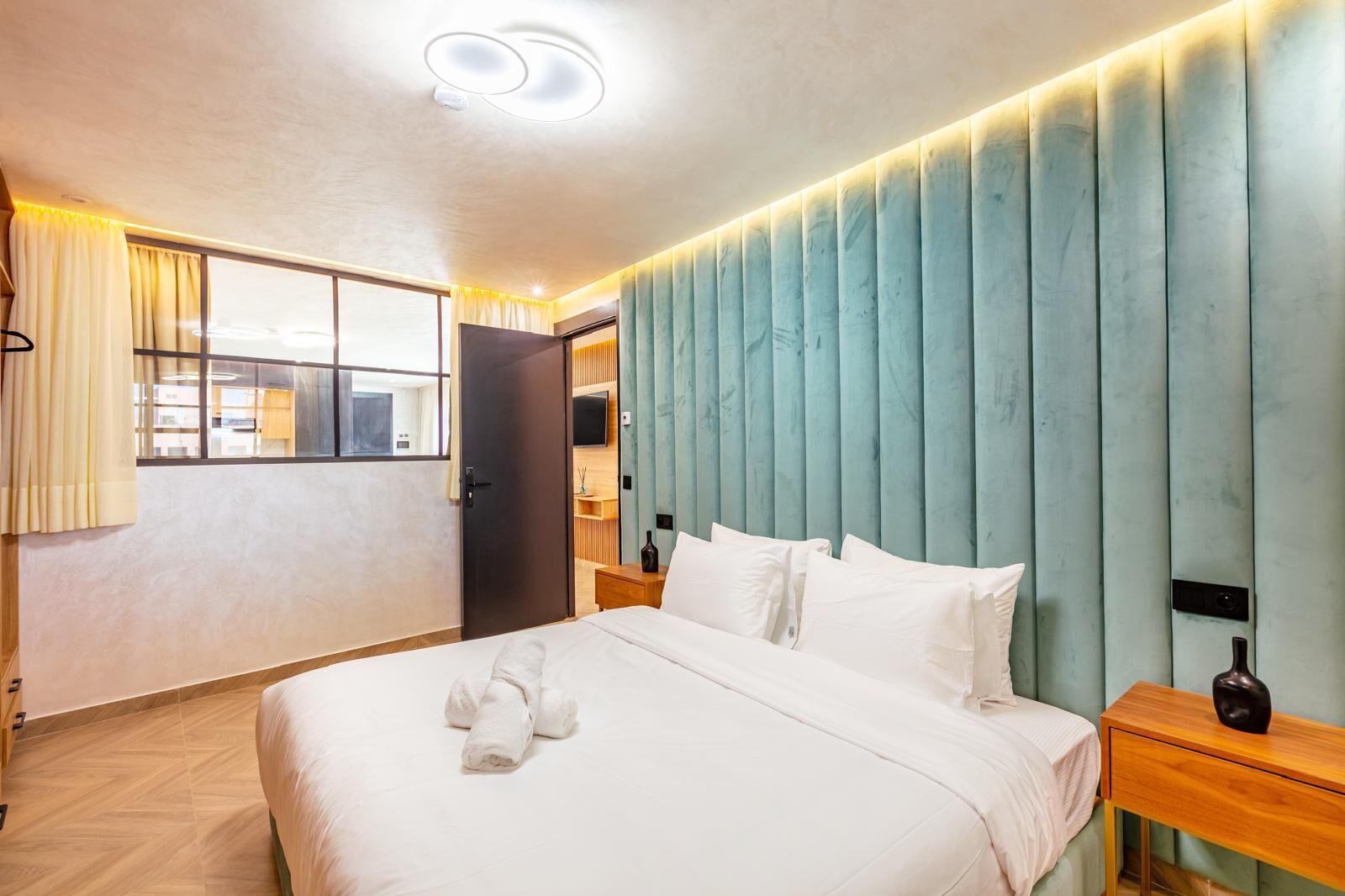 Quarto de hotel com uma cama, mesas de cabeceira, uma janela com cortinas e um painel vertical na parede.