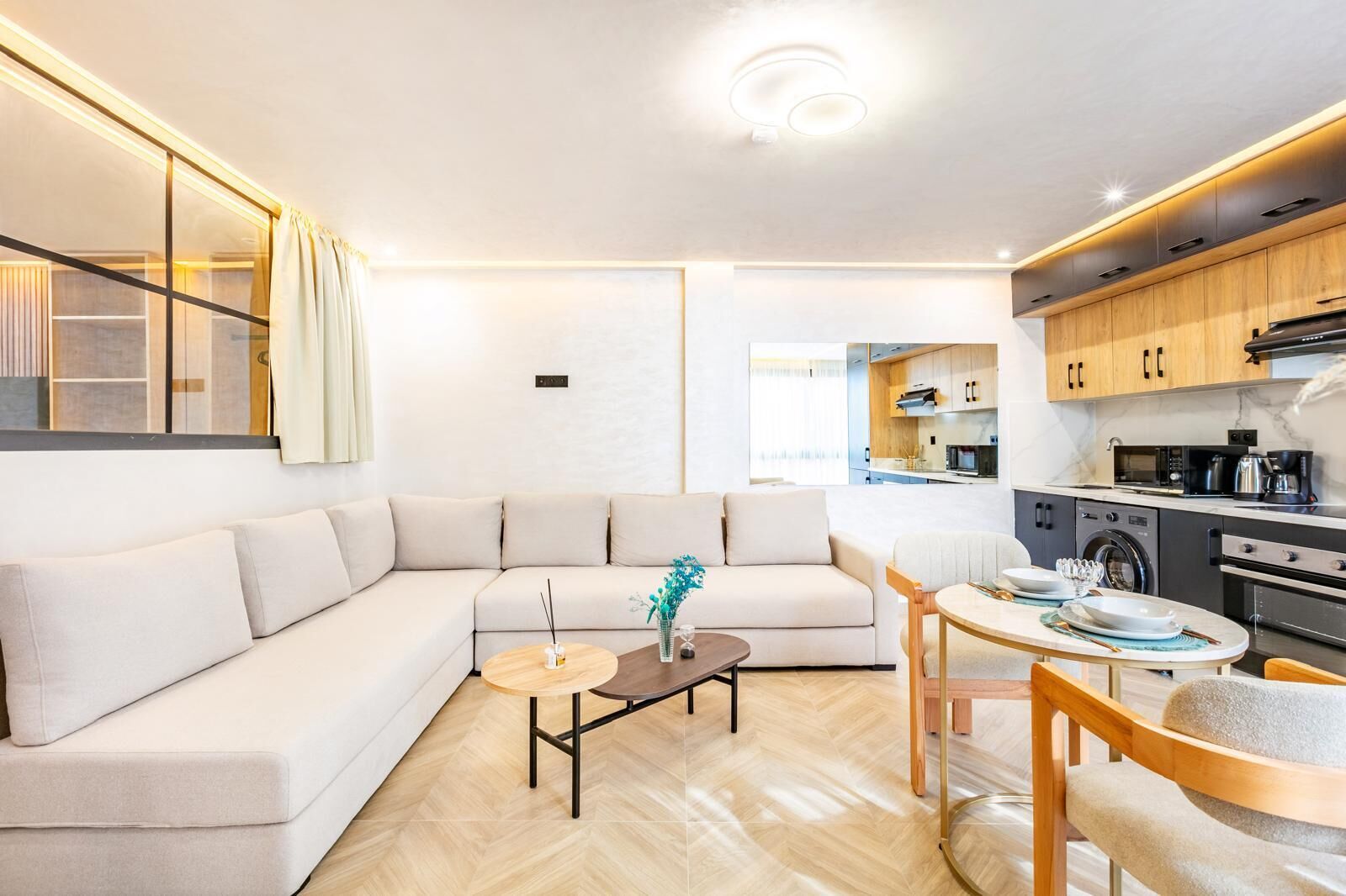 Ein modernes Wohnzimmer mit einer Couch, einem Couchtisch und einem Essbereich, verbunden mit einer Küche mit Holzschränken und Geräten.