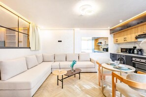 A modern living room with a sofa, coffee table, and dining area, connected to a kitchen with wooden cabinets and appliances. - LUXURY APARTH GUELIZ MARRAKECH AYLAL  (Safi)