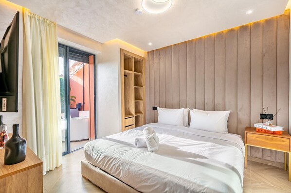 Ein modernes Hotelzimmer mit einem großen Bett, einem hölzernen Kopfteil, einem Nachttisch mit Büchern und einer Schiebetür zu einem Außenbereich.
