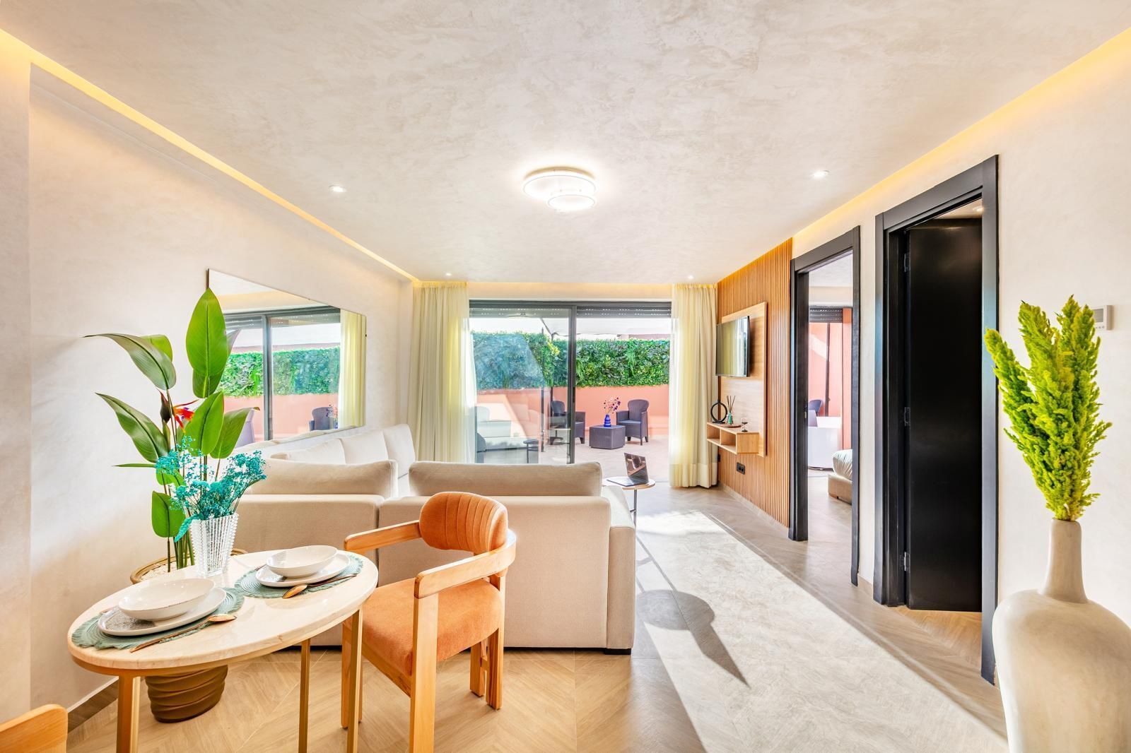 Ein modernes Hotelzimmer mit Essbereich, einer Couch, einem an der Wand befestigten Fernseher und Blick ins Freie.