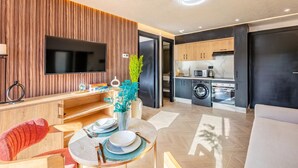 A modern living room with a flat-screen TV, wooden panel wall, dining table with plates, and a sofa. - LUXURY APARTH GUELIZ MARRAKECH AYLAL  (Safi)