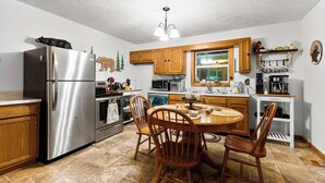A kitchen with a stainless steel refrigerator, wooden cabinets, a dining table with chairs, and a window with a view. - Mountain Mist Cottage , Valley Views , Sleeps 6 (Sevierville)