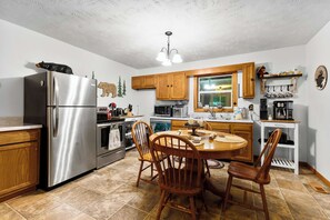 A kitchen with a stainless steel refrigerator, wooden cabinets, a dining table with chairs, and a window with a view. - Mountain Mist Cottage , Valley Views , Sleeps 6 (Sevierville)
