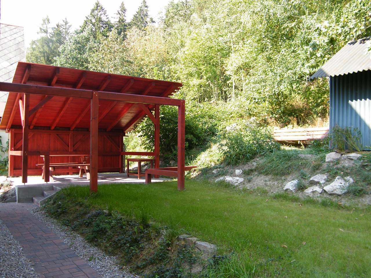 A covered picnic area with benches, a small shed, and a pathway leading to it.