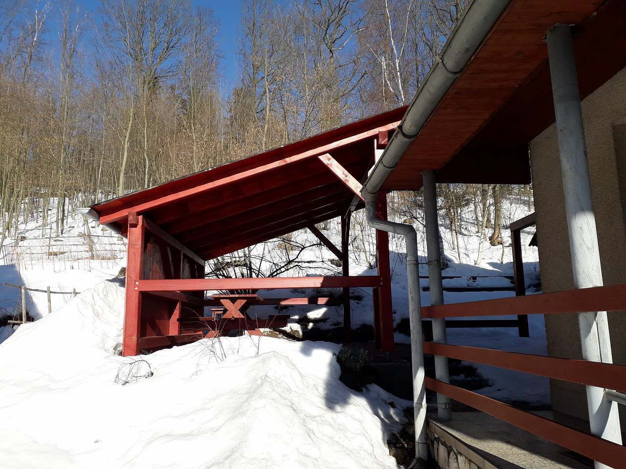 A red wooden structure with a roof, surrounded by snow and trees.