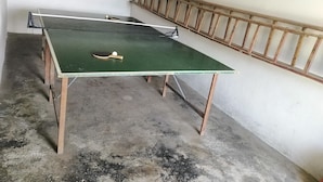 Et bordtennisbord med bold og bat i et rum med betongulv og gelænder af træ.