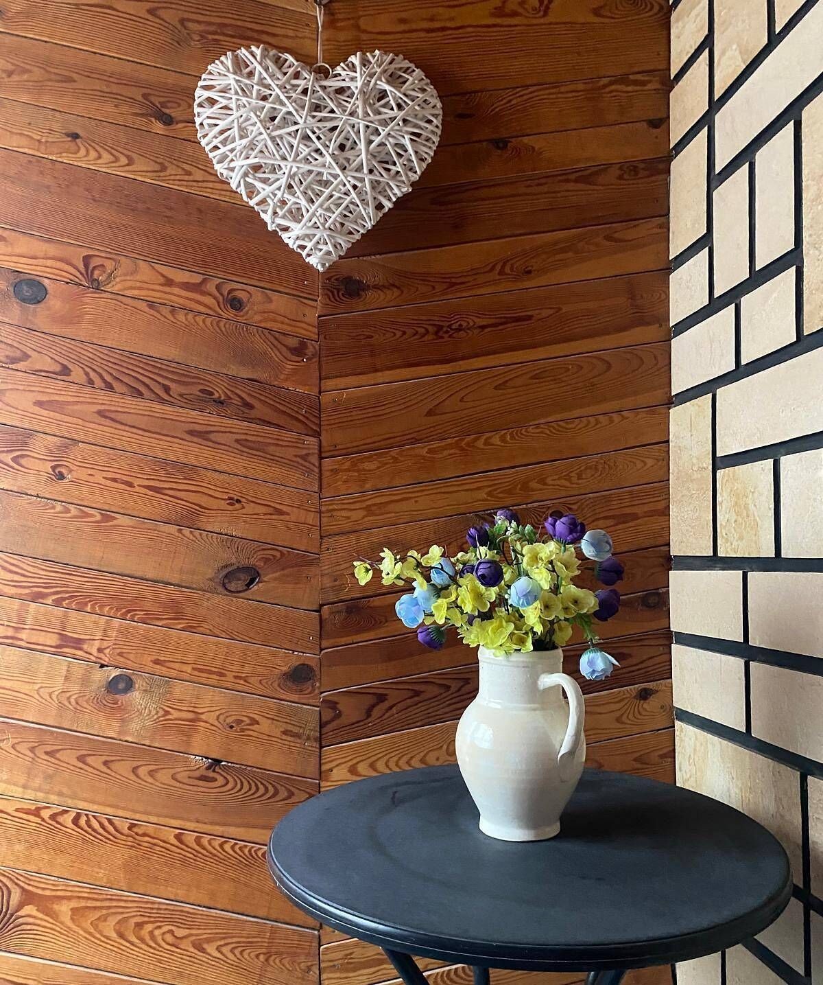 A wooden wall with a heart-shaped decoration and a vase with flowers on a small table.