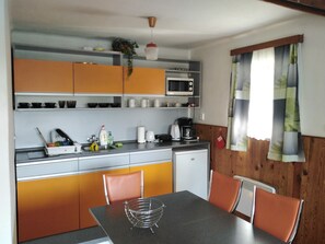 A compact kitchen with a microwave, coffee maker, and various utensils. There is a dining table with chairs and a window with curtains. - Cottage IRENA in Giant Mountains (Čistá v Krkonoších)