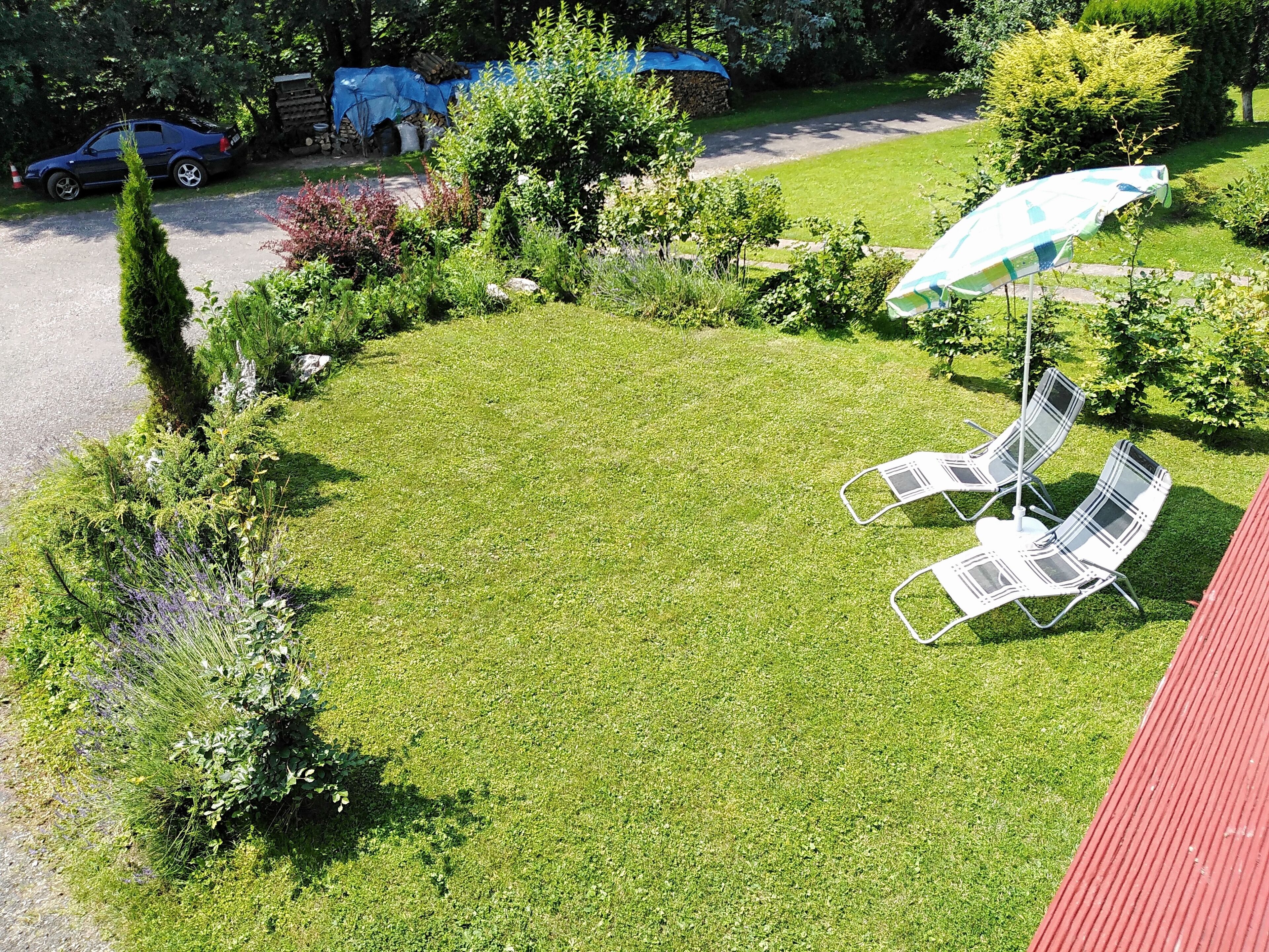 Une pelouse bien entretenue, agrémentée de deux chaises longues et d’une table, le tout entouré de divers arbustes et d’un petit arbre.