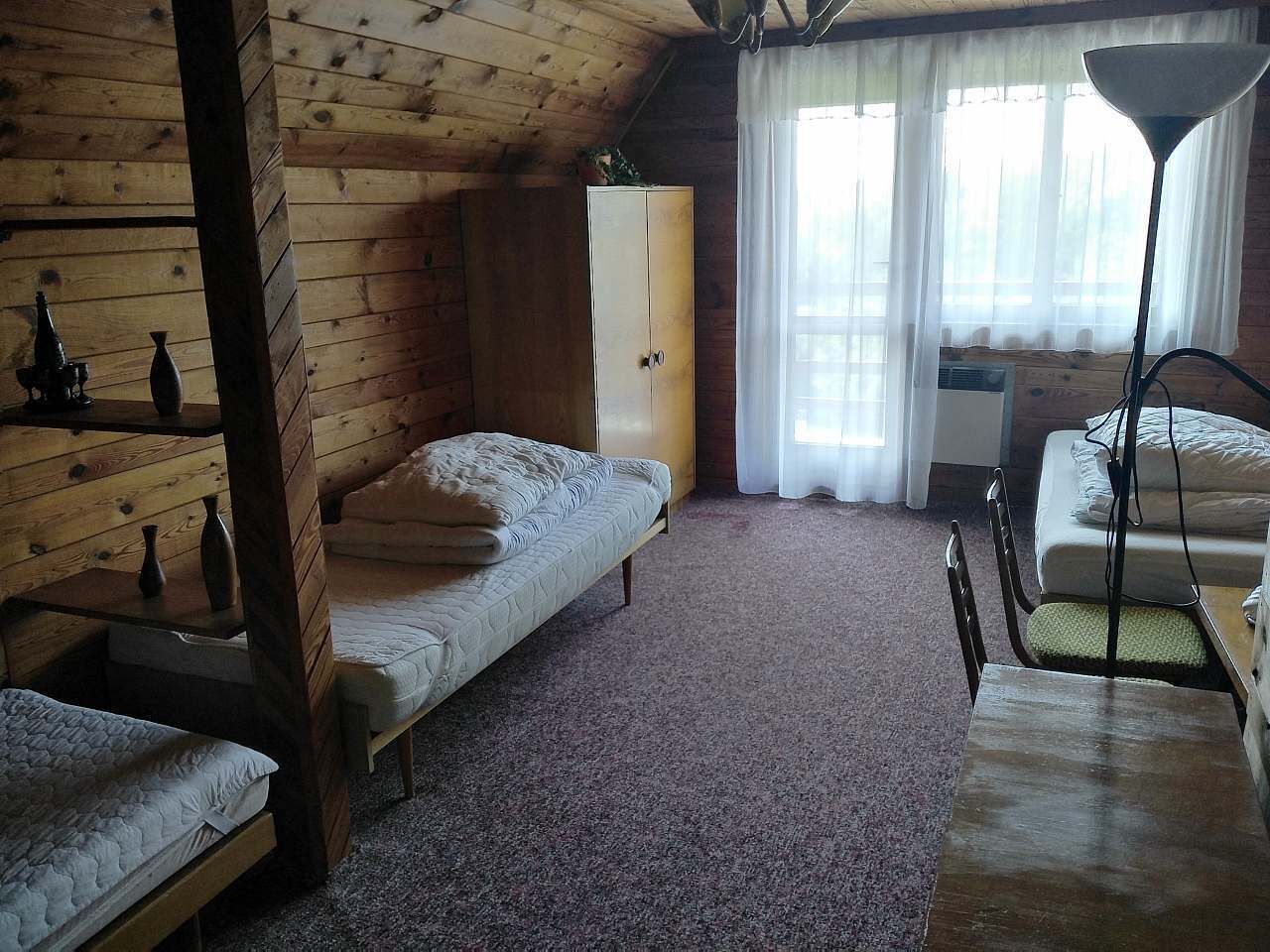 Une chambre confortable, aménagée dans le style d’un chalet, avec deux lits simples, une armoire en bois, une table et une lampe.