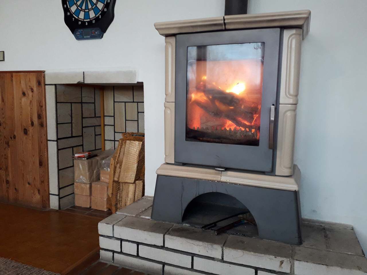 A wood-burning stove with a glass front, a dartboard, and a fireplace.