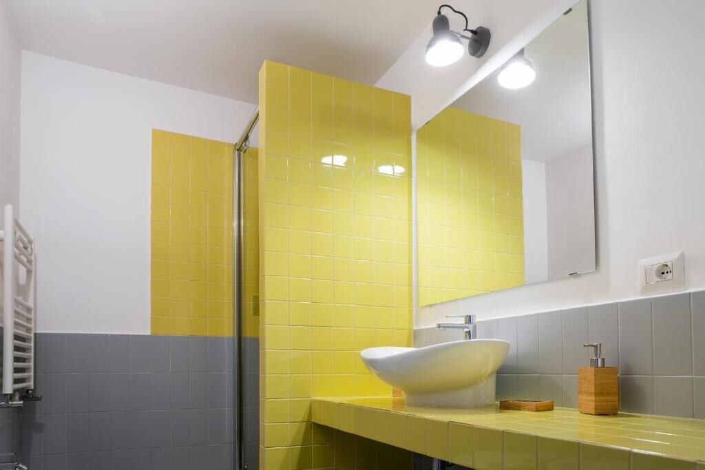 Un baño con pared de azulejos amarillos, un lavabo blanco y un espejo.