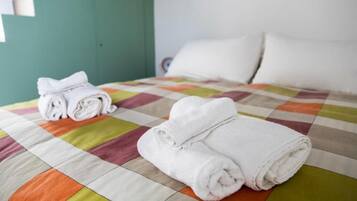 Una cama con un edredón colorido y toallas blancas dobladas con cuidado.