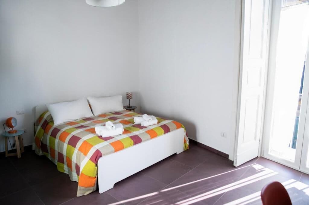 Un dormitorio con cama, mesita de noche, lámpara y vistas al exterior.