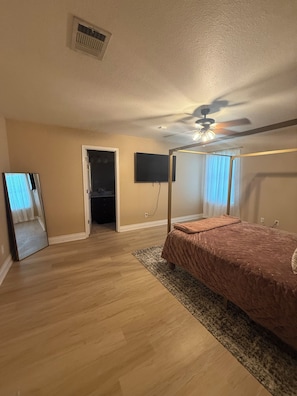 Ein Schlafzimmer mit Himmelbett, Deckenventilator, flachbildschirmfernseher an der Wand und begehbarer Kleiderschrank.