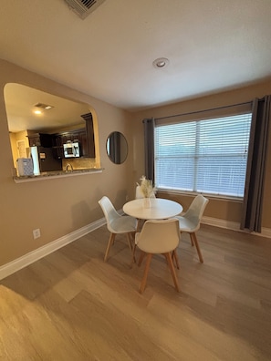 A dining area with a round table, four chairs, a mirror, and a window with blinds. - Hill Country Retreat Minutes to Gruene, Rivers & Canyon Lake (New Braunfels)