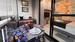A modern room with a dining table set for two, a sofa, and a large window. - Confortável Studio na Bela Vista Centro (São Paulo)