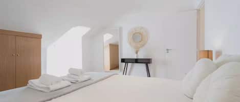 Un dormitorio con una cama, un armario de madera, una mesita con un florero y un espejo en la pared.