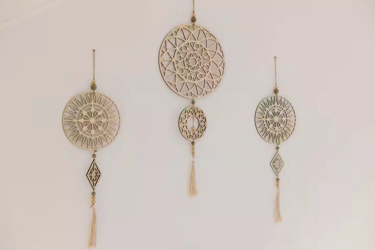 Three wall-mounted dreamcatchers with geometric patterns and tassels.