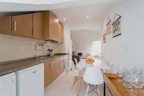 A modern kitchen with wooden cabinets, a granite countertop, and white appliances. - Casa Trinitária · 3BR/1WC · Sleeps 8 · Central (Lisboa)