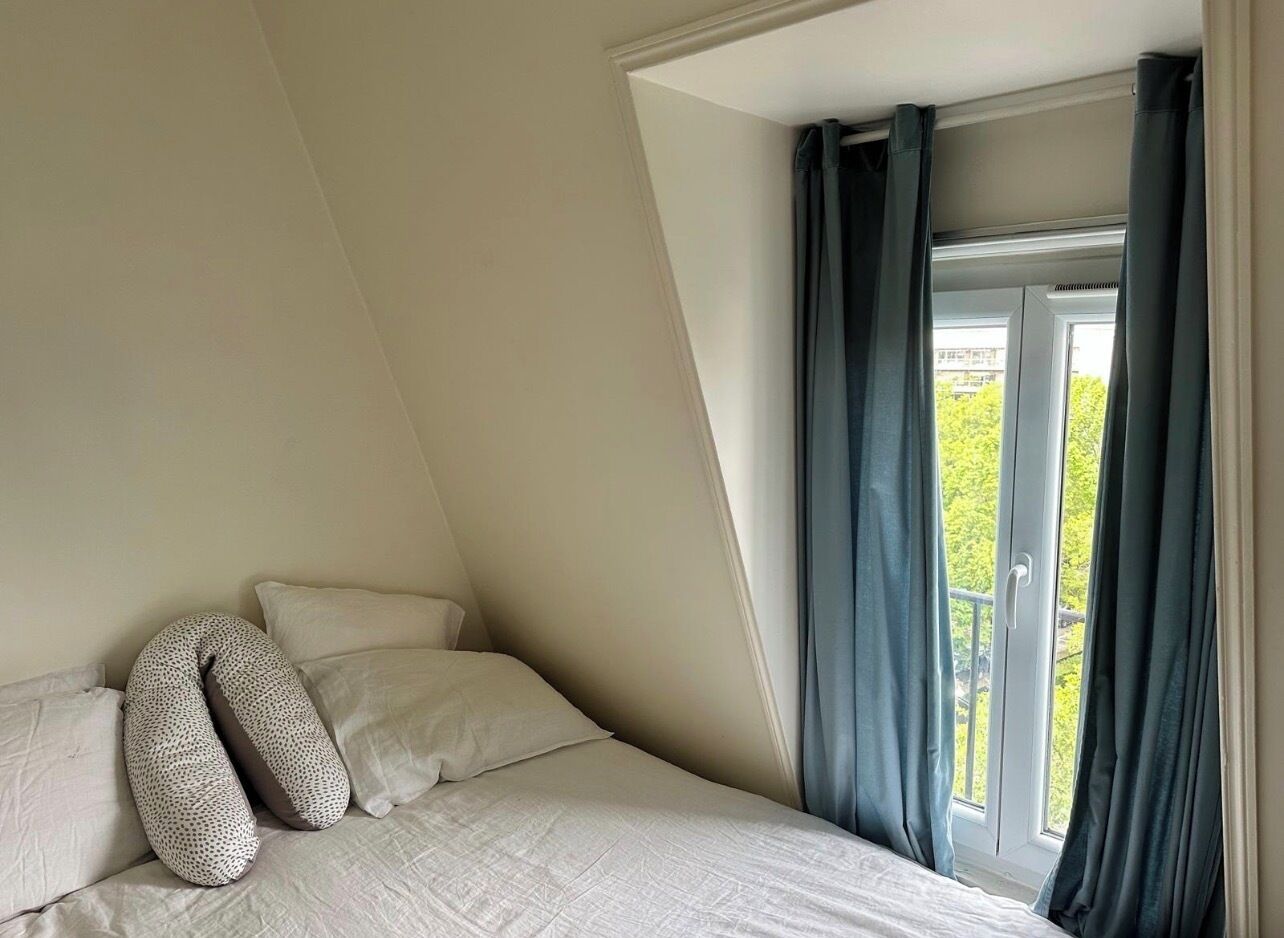 Una camera da letto con soffitto spiovente, un letto con biancheria bianca, due cuscini e una finestra con tende.