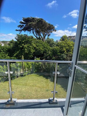 A balcony with a glass railing overlooking a grassy area with trees and a clear sky. - New Stunning House St Ives With Parking (St Ives)
